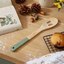 Cartco Cooksmart Forest Fable bamboo spoon with sage green handle and woodland leaf cutouts on a wooden kitchen table