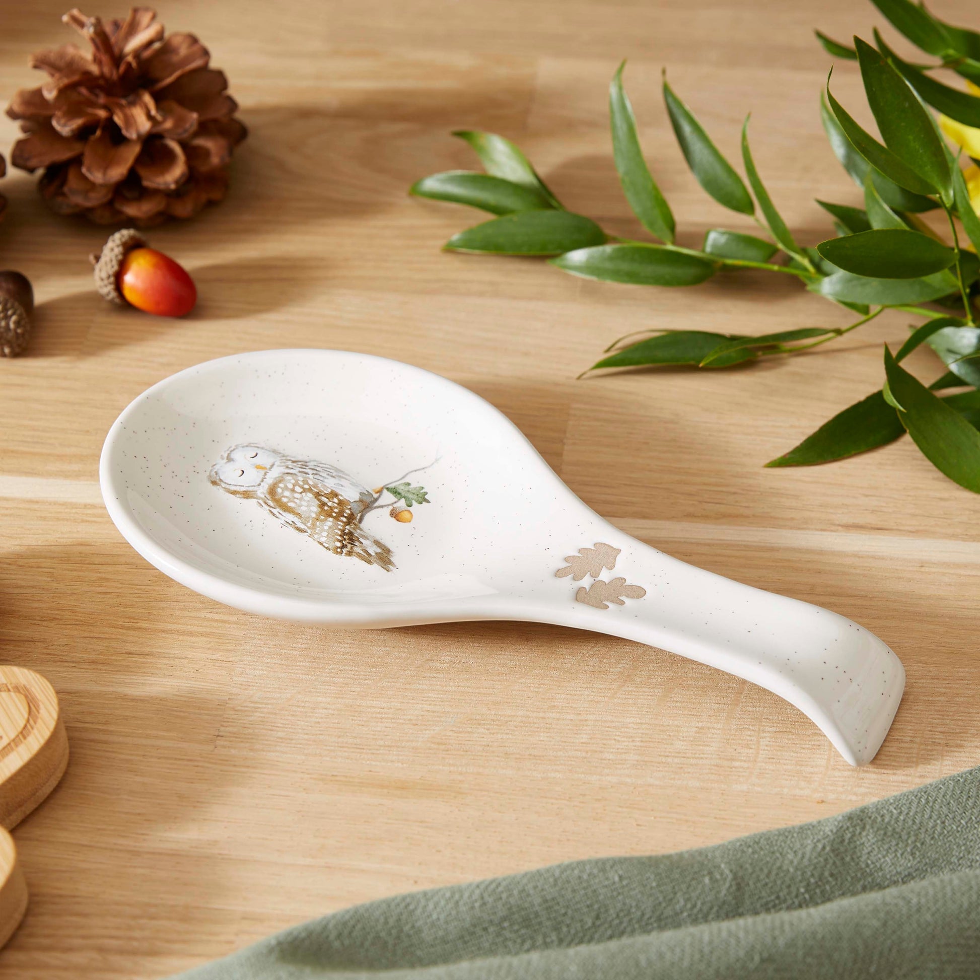 Cartco Cooksmart Forest Fable ceramic spoon rest with a speckled cream finish, owl illustration, and oak leaf detail.