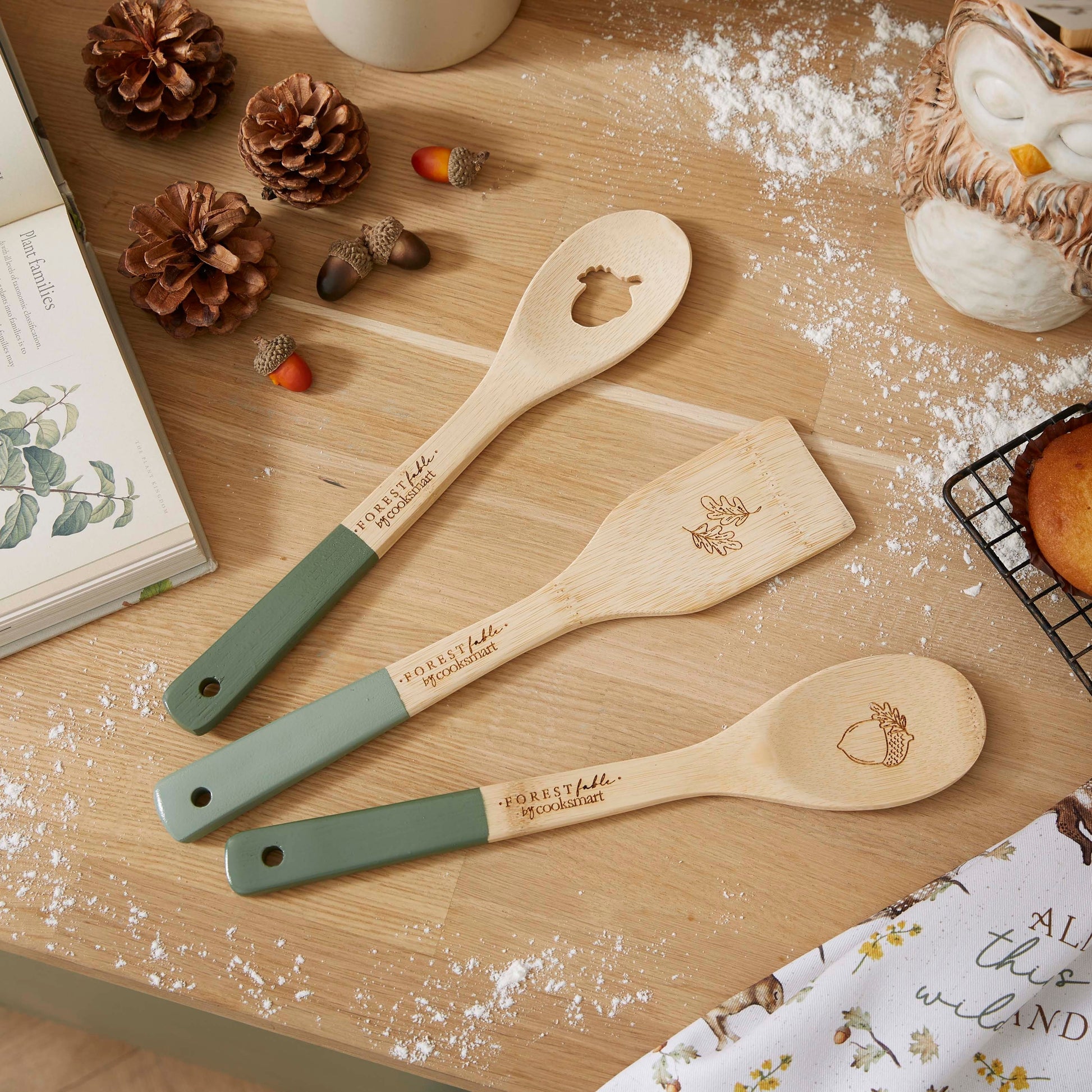 Cartco Forest Fable bamboo utensil set featuring sage green handles and woodland animal engravings on a wooden table
