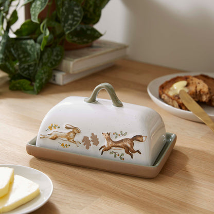 Cartco ceramic butter dish with cream speckled cover, hare and fox illustration, and sage green handle on wooden table