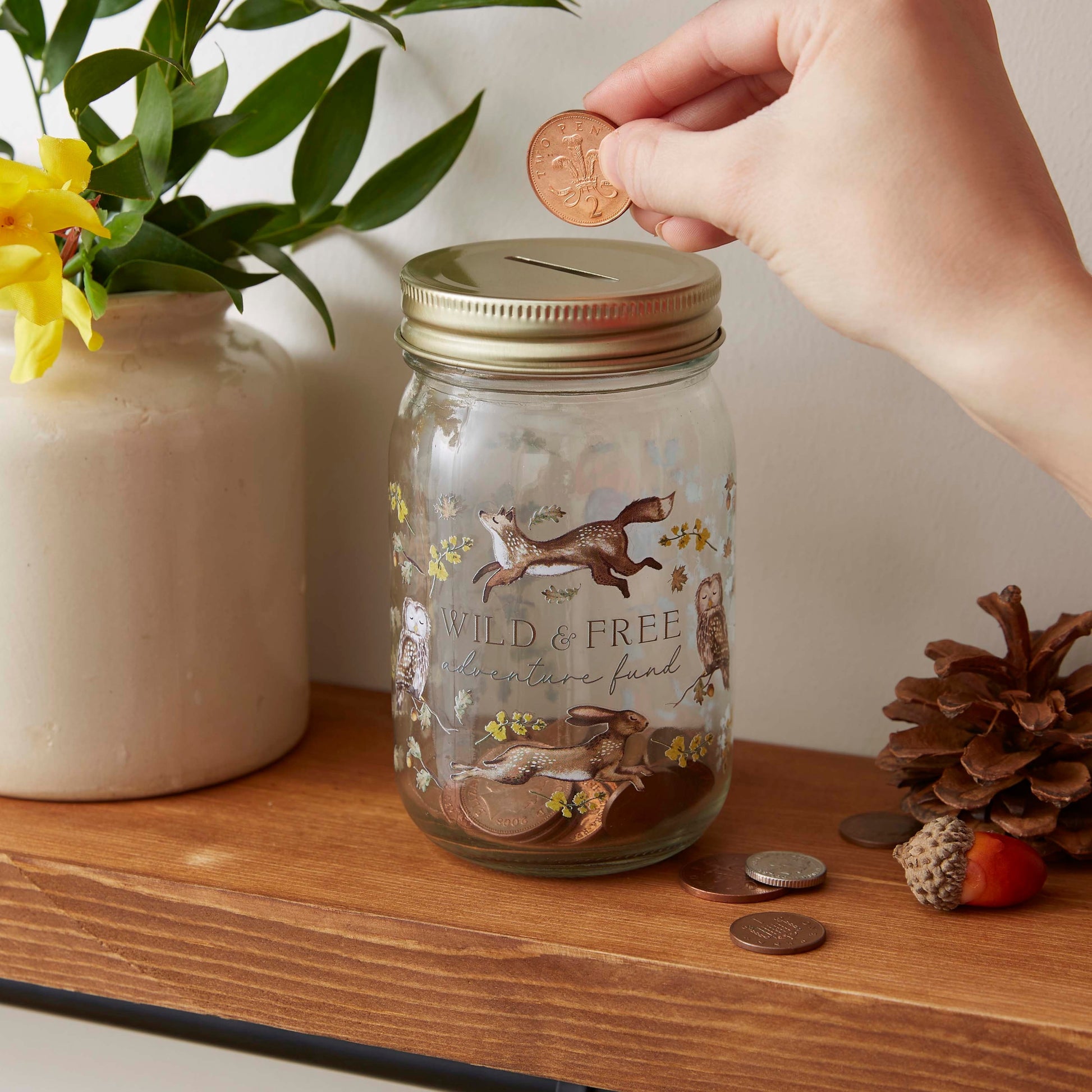 Cartco Cooksmart Forest Fable ceramic money jar with woodland animal illustrations and a gold lid on a wooden shelf