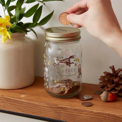Cartco Cooksmart Forest Fable ceramic money jar with woodland animal illustrations and a gold lid on a wooden shelf