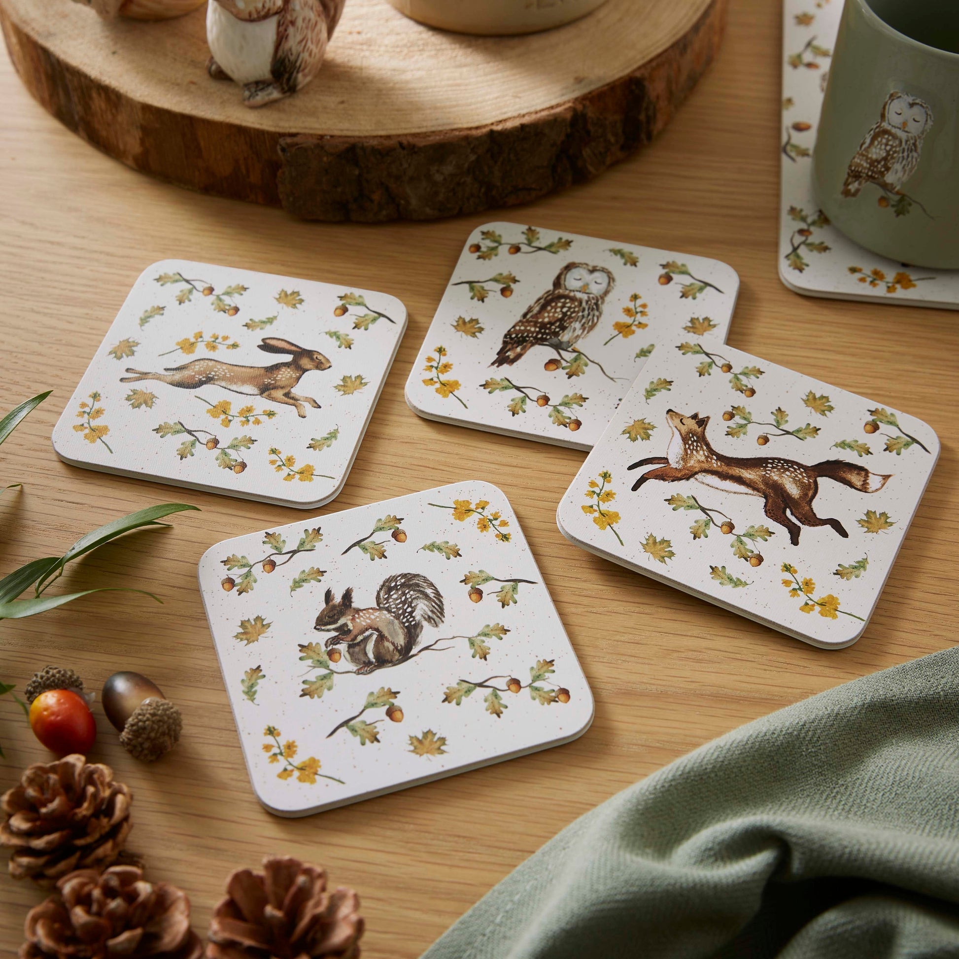 Cartco Cooksmart Forest Fable square coasters featuring hare, owl, fox, and squirrel illustrations on a wooden table.