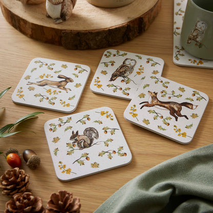 Cartco Cooksmart Forest Fable square coasters featuring hare, owl, fox, and squirrel illustrations on a wooden table.