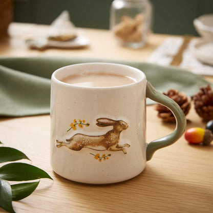 Cartco speckled cream ceramic mug featuring a running hare illustration with sage green handle on a wooden table.