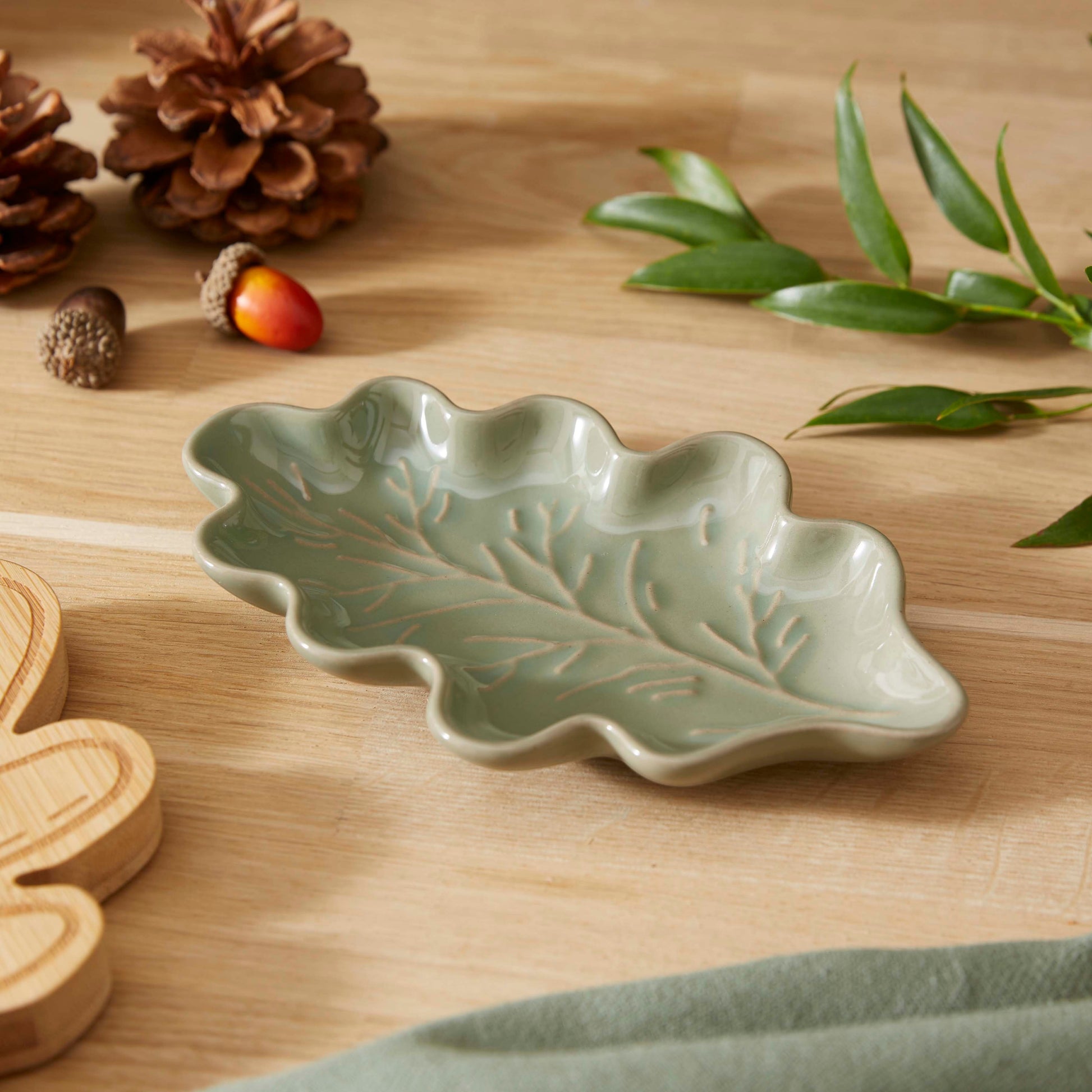 Cartco sage green ceramic spoon rest shaped like an oak leaf with embossed vein detailing on a wooden kitchen surface.